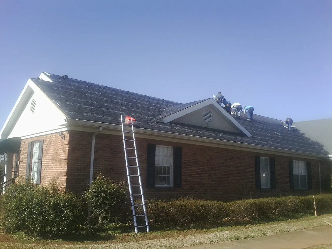 Crew tearing shingles off a brick ranch roof with a ladder set — Emergency Roof Repair work by our crew in Bergton