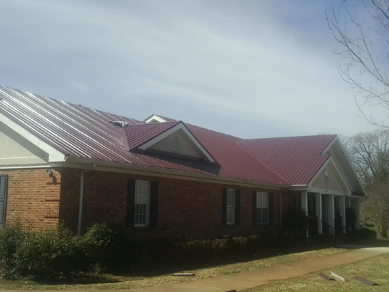 Red metal roof with gabled entries on a long brick building, from a Hail Damage Roof Repair job in Bergton