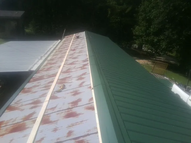 Old rusted panels beside newly installed green metal roofing — Wind Damage Roof Repair by Roofing Brothers in Bergton