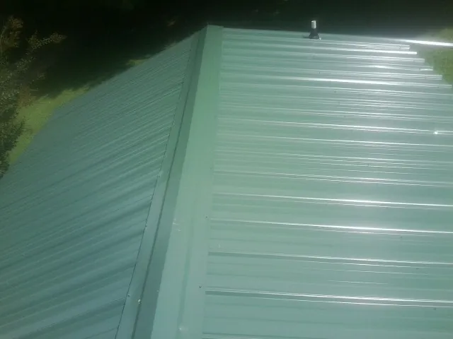 New green metal panels meeting at the ridge of a roof — Flat Roof Repair work by our crew in Bergton
