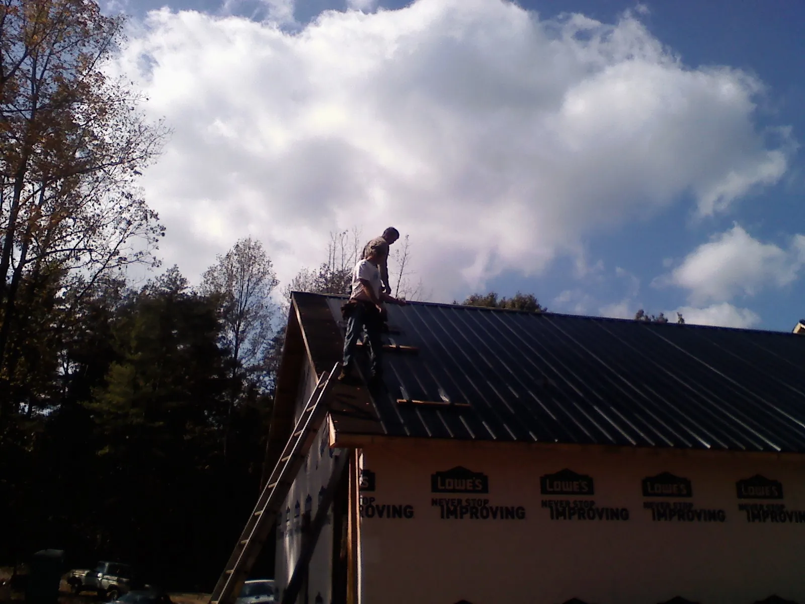 Roofer fastening dark metal panels high against a cloudy sky, from a Roof Inspection job in Bergton