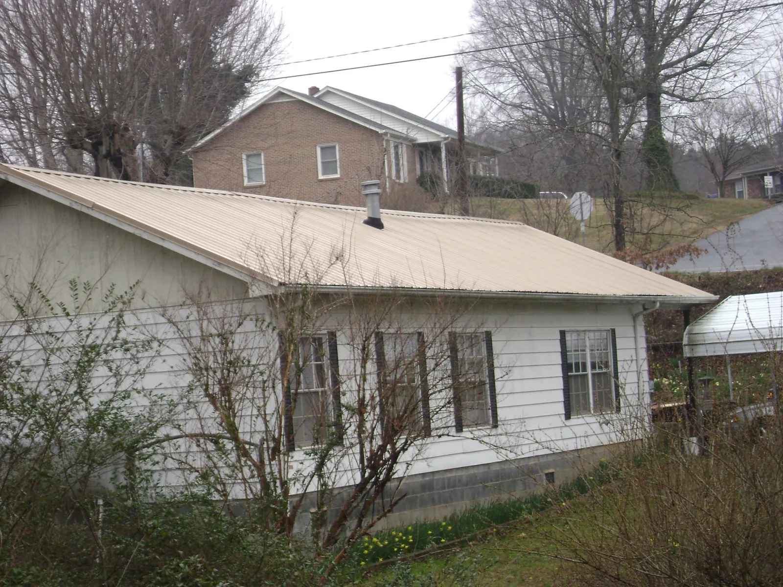 Tan metal roof on a white sided house set into a hillside — Commercial Roofing by Roofing Brothers in Bergton